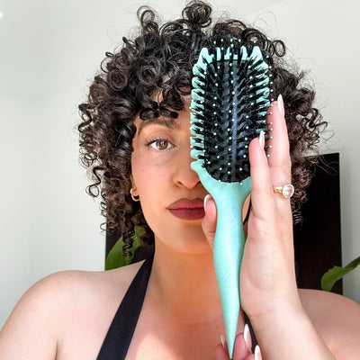 Frau mit definierten Locken hält die CurlDefine Lockenbürste mit veganen Borsten vor das Gesicht – für Volumen, Kontrolle und frizzfreies Styling
